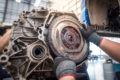 Hands of a car mechanic pulling on a dual mass clutch during clutch replacement